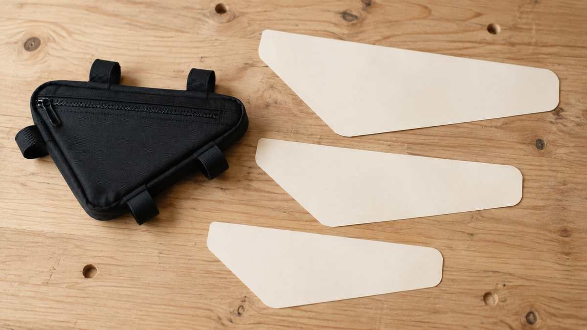 Schwarze Rahmentasche neben drei blanken Papierformen auf einem Holztisch