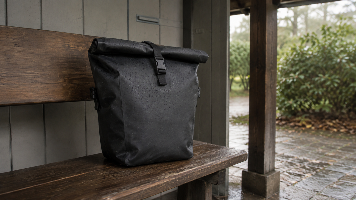 Geschlossene schwarze Rolltop-Tasche mit Wassertropfen auf einer Holzbank