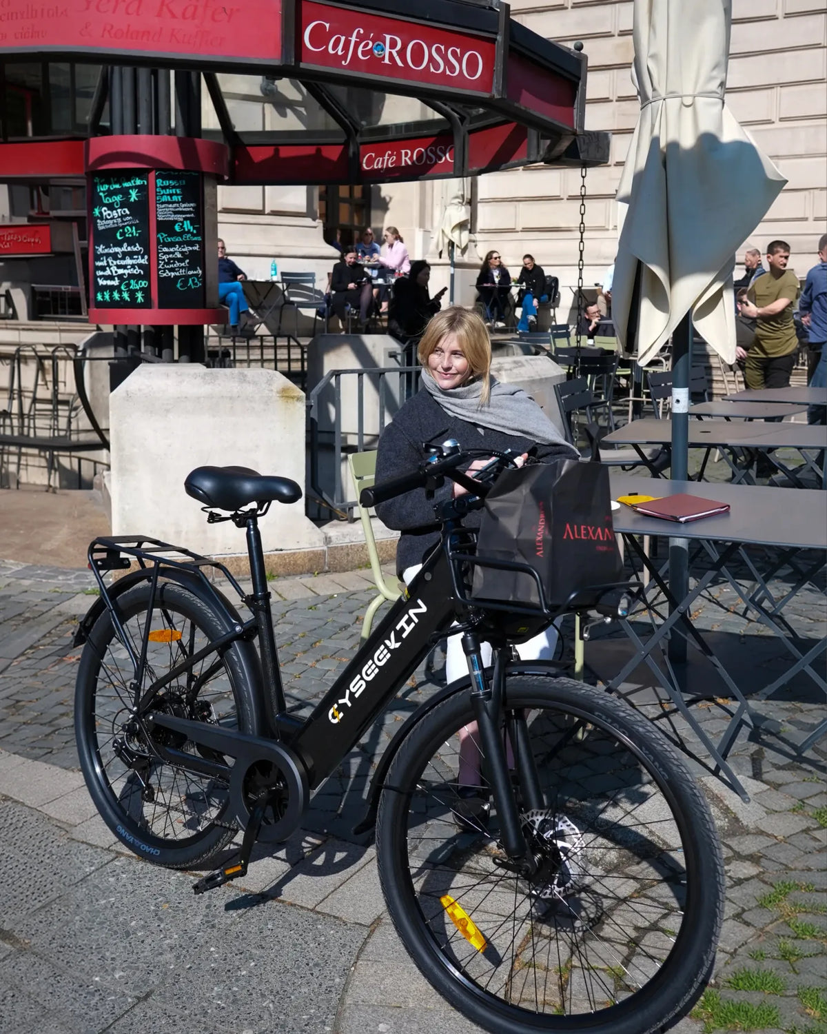 Frau macht mit ihrem Cyseekin E-Bike eine Pause vor einem Stadtcafé